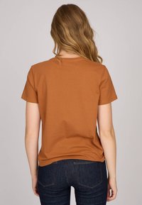 T-shirt à manches courtes, couleur rouille, avec col rond, en matériau doux et coupe décontractée, associé à un jean en denim foncé.
