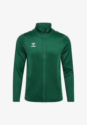 Groene jas met ritssluiting gemaakt van glad polyester, voorzien van een hoge kraag, zijzakken en witte strepen op de schouders. Hummel-logo op de borst.