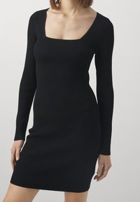 Abito in maglia a coste nera con scollatura quadrata, maniche lunghe e silhouette aderente, caratterizzato da una superficie testurizzata e lunghezza mini.