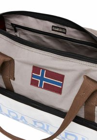 Borsa in tela con interno grigio, cerniera nera, manici marroni e un'etichetta in tessuto rossa con la bandiera norvegese. Logo "NAPAPIJRI" visibile.
