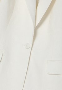 Witte linnen blazer details omvatten een enkele knoopsluiting, voorzakken en een textiel met textuur. Schoon ontwerp met een gestructureerde vorm.