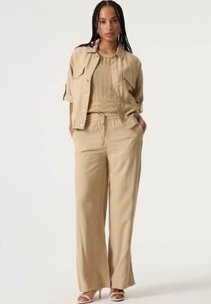 Beiges zweiteiliges Outfit bestehend aus einem kurzärmligen Hemd mit Knöpfen und weiten Hosen. Das Stricktop sorgt mit einem gemusterten Design für Struktur.