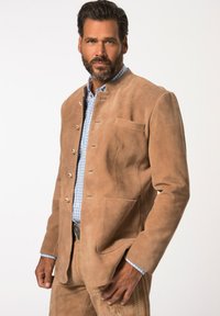 Giacca di suede marrone chiaro con colletto rialzato, bottoni dorati e taschino sul petto; abbinata a una camicia a quadri blu.