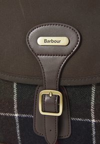 Bruine en geruite stoffen tas met leren schouderband en messing gesp, voorzien van een metalen plaat met de gegraveerde merknaam "Barbour".