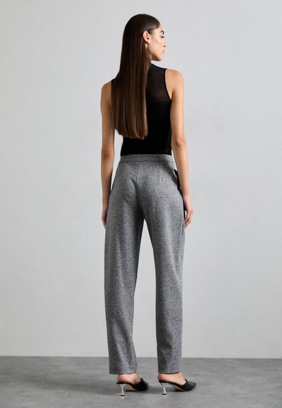 Grau-karierter Hosen mit hoher Taille, Eingrifftaschen und entspannter Passform. Kombiniert mit einem eng anliegenden schwarzen ärmellosen Top und offenen Sandalen.