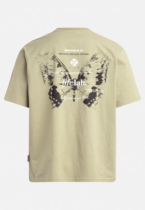 Khaki koszulka z dużym czarnym motylem na plecach, z białymi i czarnymi detalami tekstowymi, krótkimi rękawami i luźnym krojem.