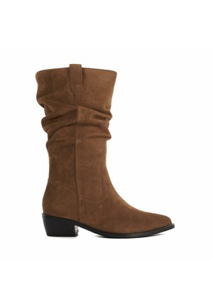 Botte en daim marron hauteur genou avec un haut légèrement affaissé, un bout arrondi et un petit talon carré. Détails avec des accents de couture subtils.