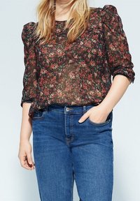 Florale durchsichtige Bluse mit Puffärmeln in dunklen Tönen, kombiniert mit blauen Denim-Jeans. Der Stoff hat ein leichtes, strukturiertes Design.