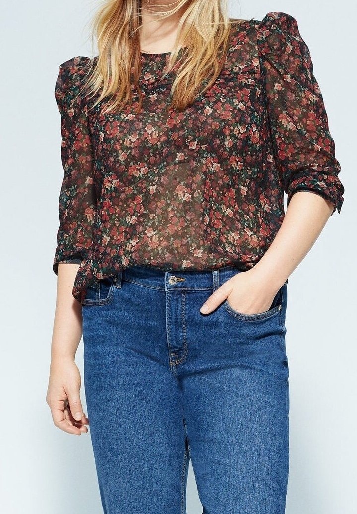 Florale durchsichtige Bluse mit Puffärmeln in dunklen Tönen, kombiniert mit blauen Denim-Jeans. Der Stoff hat ein leichtes, strukturiertes Design.