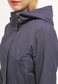 Navy blue hooded jacket with a smooth texture, snap button closures, and a front pocket. Features a fitted design with a slight sheen.