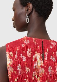 Abito rosso a fiori con texture arricciata e dettagli con aperture a chiave sul retro. Orecchini geometrici argentati completano il look.