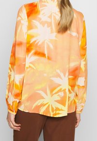 Koszula z długim rękawem wykonana z lekkiego materiału, z pomarańczowym i żółtym nadrukiem palm, o luźnym kroju i marszczonymi rękawami.