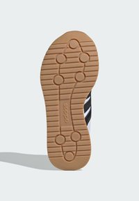 Podošva topánky s hnedou gumovou textúrou, s vzorom horizontálnych drážok a kruhových trakčných bodov. Viditeľné biele a čierne akcenty.