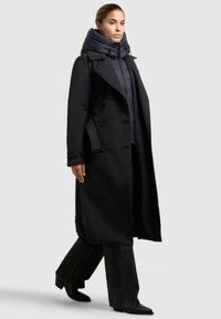 Zwarte double-breasted trenchcoat met een puffy capuchonvoering, met een gladde textuur en een getailleerde pasvorm, gecombineerd met wijde zwarte jeans en hakken.