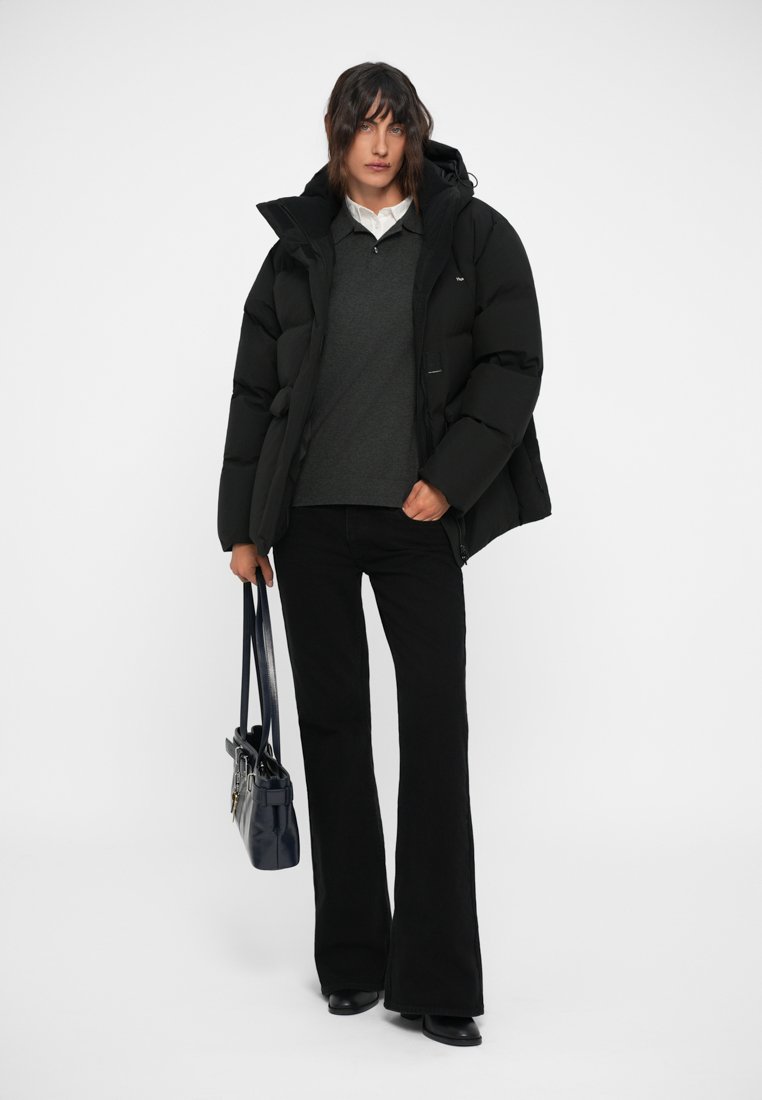 Black puffer jacket with a hood, layered over a dark gray sweater and white collared shirt. Worn with black flared trousers and carrying a dark bag.