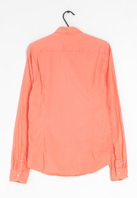 Camisa coral de manga larga colgada en una percha, con un cuello de botón, textura suave y puños abotonados, con un ligero brillo.