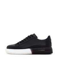 Sneaker noir en cuir avec un bout rond, un design sobre, une semelle en caoutchouc blanche et un accent de talon de couleur sombre contrastante. Doté d'un système de laçage.