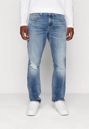 Jeans in denim blu chiaro con una vestibilità ampia, caratterizzati da un dettaglio di strappi al ginocchio, cinque tasche e cuciture accentuate. Abbinati a sneakers bianche.