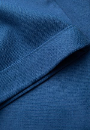 Niebieska tkanina z teksturowanym splotem, z zagiętym brzegiem i gładkim wykończeniem. Widoczne przeszycia wzdłuż zagięcia dodają szczegółów.