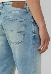 Lichtblauwe denim jeans met een vervaagde afwerking, voorzien van een bruine leren patch, een klassiek zakontwerp en subtiele stikseldetails.