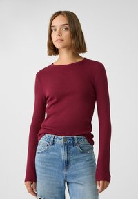 Bordeaux lange mouwen rib top met een ronde hals, gecombineerd met lichtblauwe distressed jeans met een knoopsluiting en vijf zakken.