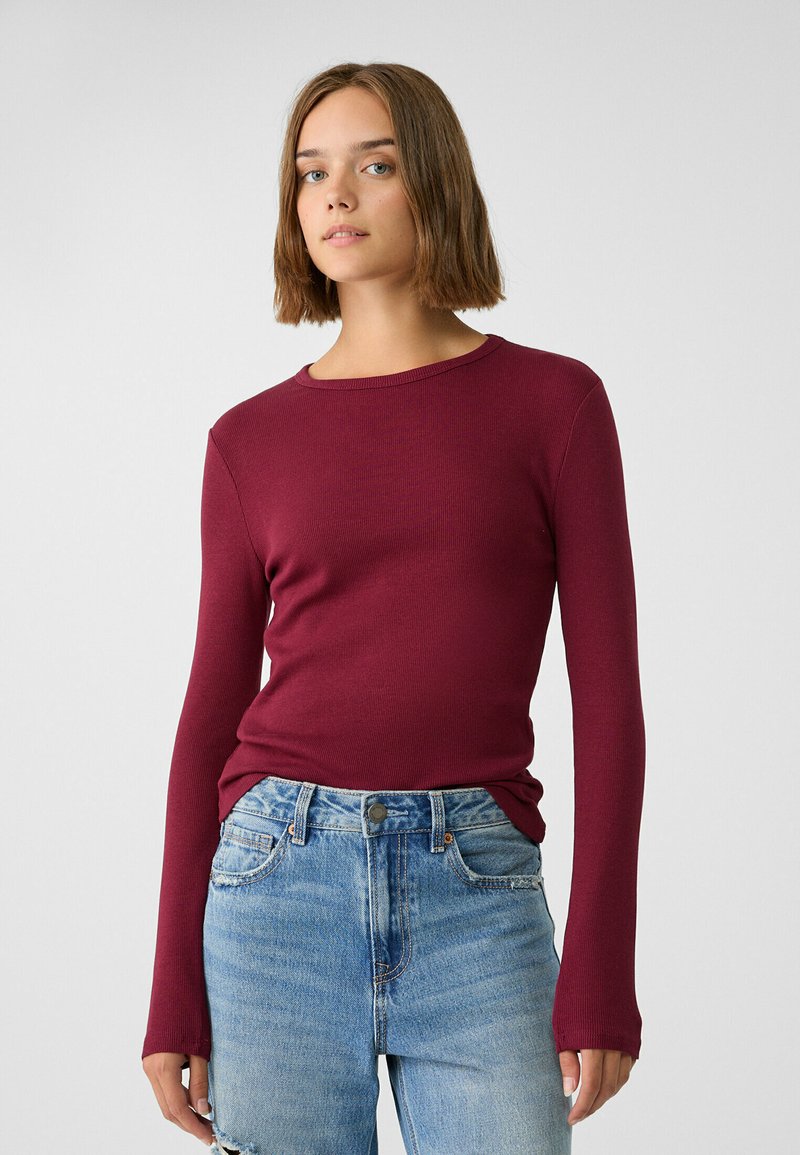 Bordeaux lange mouwen rib top met een ronde hals, gecombineerd met lichtblauwe distressed jeans met een knoopsluiting en vijf zakken.