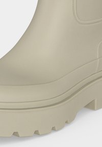 Gros plan de la semelle et du côté d'une botte en caoutchouc beige avec un motif de semelle épais et rainuré.