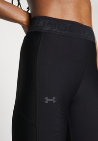 Zbliżenie na osobę ubraną w czarne rajstopy kompresyjne Under Armour, na udzie widoczny logo oraz markowy pas.