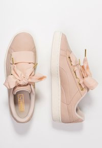 Baskets en daim rose avec des lacets en ruban noués en nœuds, des accents de quincaillerie de couleur dorée et des semelles en caoutchouc blanches à motifs texturés.