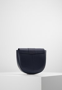 Borsa a tracolla in pelle blu navy con forma arrotondata, texture liscia e chiusura piatta. Presenta dettagli cuciti lungo i bordi.