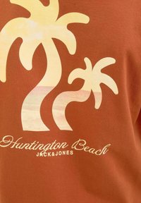 Ruda marškinių su stylizuotais geltonais palmėmis ir tekstu "Huntington Beach JACK&JONES", švelni tekstūra ir kasdieniškas dizainas.