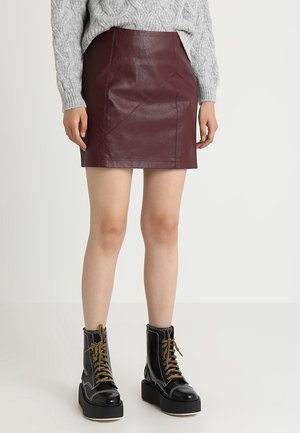 Person iført en bordeaux læder mini nederdel, grå kabelstrikket sweater og sorte platform snørestøvler, stående på en hvid baggrund.