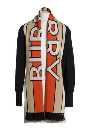 Jersey negro con una larga bufanda beige y naranja con letras grandes y gruesas y flecos negros en los extremos, colocada sobre los hombros.