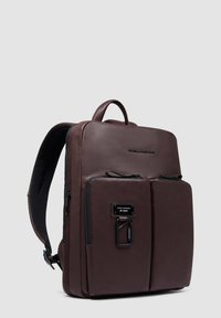 Mochila de cuero marrón con un diseño elegante, dos bolsillos frontales, un asa superior y correas de hombro ajustables. Superficie texturizada con cremalleras.