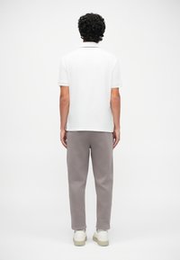 Cămașă polo albă cu guler negru, asortată cu pantaloni de trening gri deschis. Ținuta este completată cu adidași albi.
