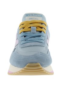 Lichtblauwe sneaker met gele en blauwe veters, een roze zijstreep en een label met "victoria since 1915" op de tong, gezien vanaf de voorkant.