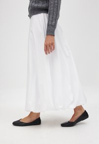 Gonna bianca, lunga fino al ginocchio, con un design fluido, abbinata a scarpe nere, piatte. La parte superiore è costituita da un maglione lavorato a maglia grigia, con texture.