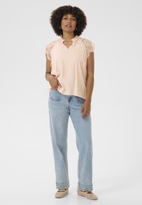 T-shirt pesc peach con maniche in pizzo, design a scollo a V, abbinato a jeans a gamba larga blu chiaro e scarpe slip-on beige. Outfit semplice e casual.