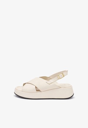 Kremowy sandał na platformie z krzyżującymi się paskami, odkrytymi palcami, regulowanym paskiem wokół kostki z złotą klamrą oraz czarną krawędzią podeszwy.