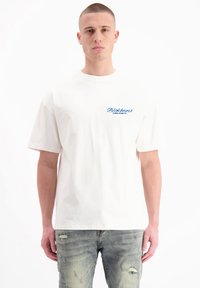 Witte katoenen t-shirt met een ronde hals, korte mouwen en een blauw tekstlogo op de linkerborst; gecombineerd met lichtblauwe versleten jeans.