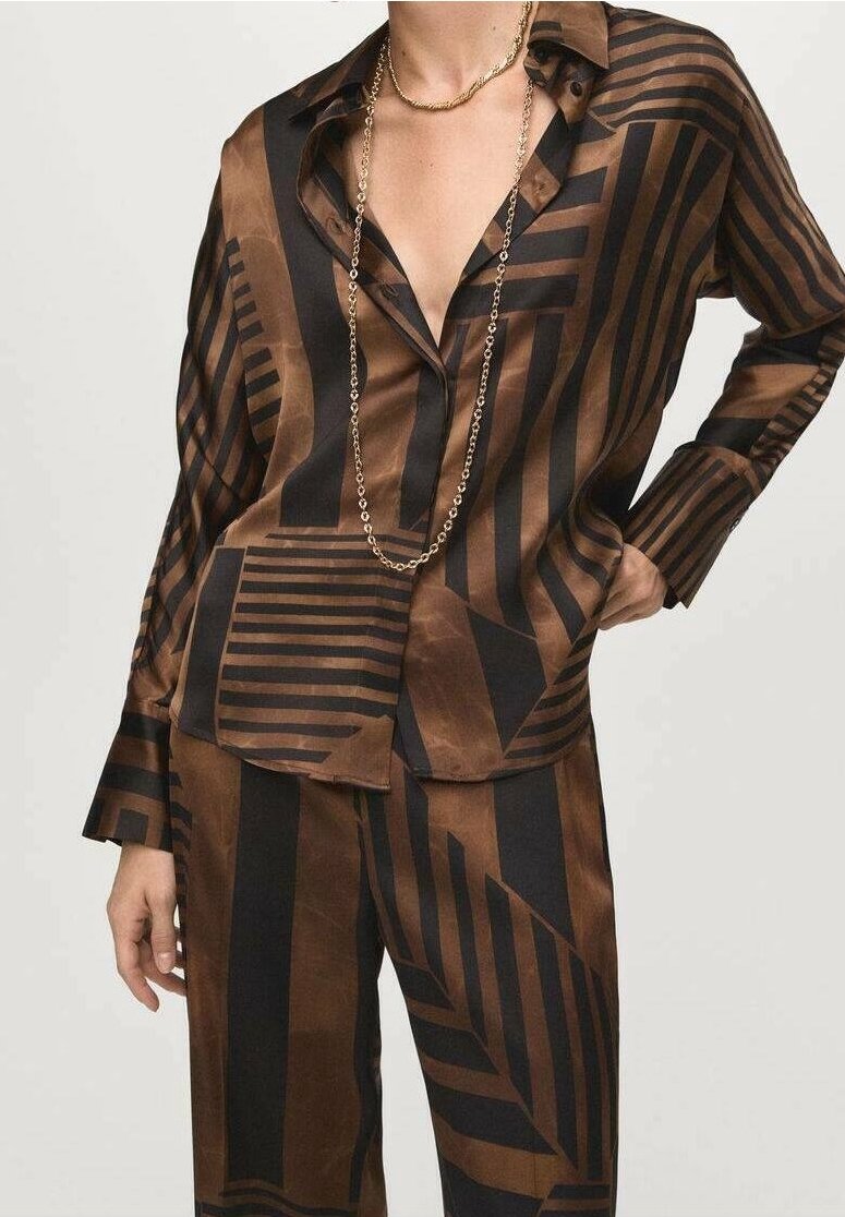 Chemise en satin rayée géométrique marron et noire et pantalon assorti, portée avec un collier chaîne en or, main posée sur la hanche.