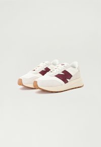 Baskets blanches et bordeaux avec une tige texturée, un système de laçage et une semelle en caoutchouc beige. Logo distinctif sur le côté.