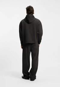 Sudadera con capucha de color gris oscuro combinada con pantalones sueltos del mismo tono, confeccionados en tela suave con textura mate; incluye capucha y bolsillo lateral en los pantalones.