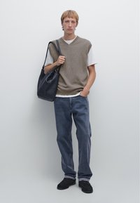 Brown knit vest over a white t-shirt, blue denim jeans, and black footwear. Holds a black leather bag with a textured finish.