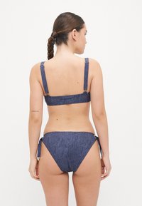 Denim stof bikini set in donkerblauw met verstelbare bandjes en striksluiting op de heupen; zachte textuur met een minimalistisch design.