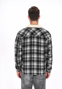 Camisa de franela a cuadros en blanco y negro con cuello de sherpa crema, puños abotonados y un ajuste relajado. Costuras visibles y acabado texturizado.