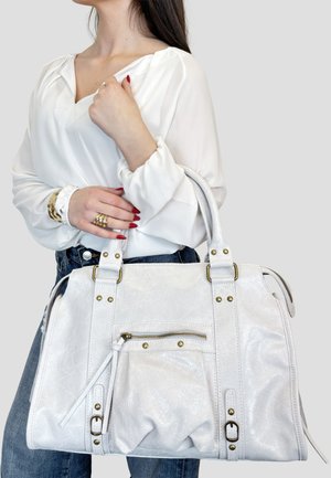 Donna con camicetta bianca e jeans blu che tiene una grande borsa a tracolla in pelle bianca con ferrature in ottone.