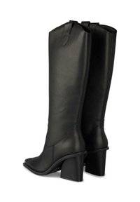 Botas de cuero negras hasta la rodilla con punta afilada, tacón grueso de bloque y un detalle de costura mínima. Presentan una etiqueta en forma de lazo en la parte superior.