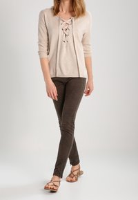 Beige lace-up sweater with a relaxed fit, paired with dark brown skinny pants and strappy sandals. Simple, textured fabric and casual design.