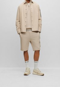 Beige avslappnad outfit bestående av en zip-up skjorta, en crewneck sweatshirt och shorts. Kompletterad med matchande skor och strumpor med logotyp.